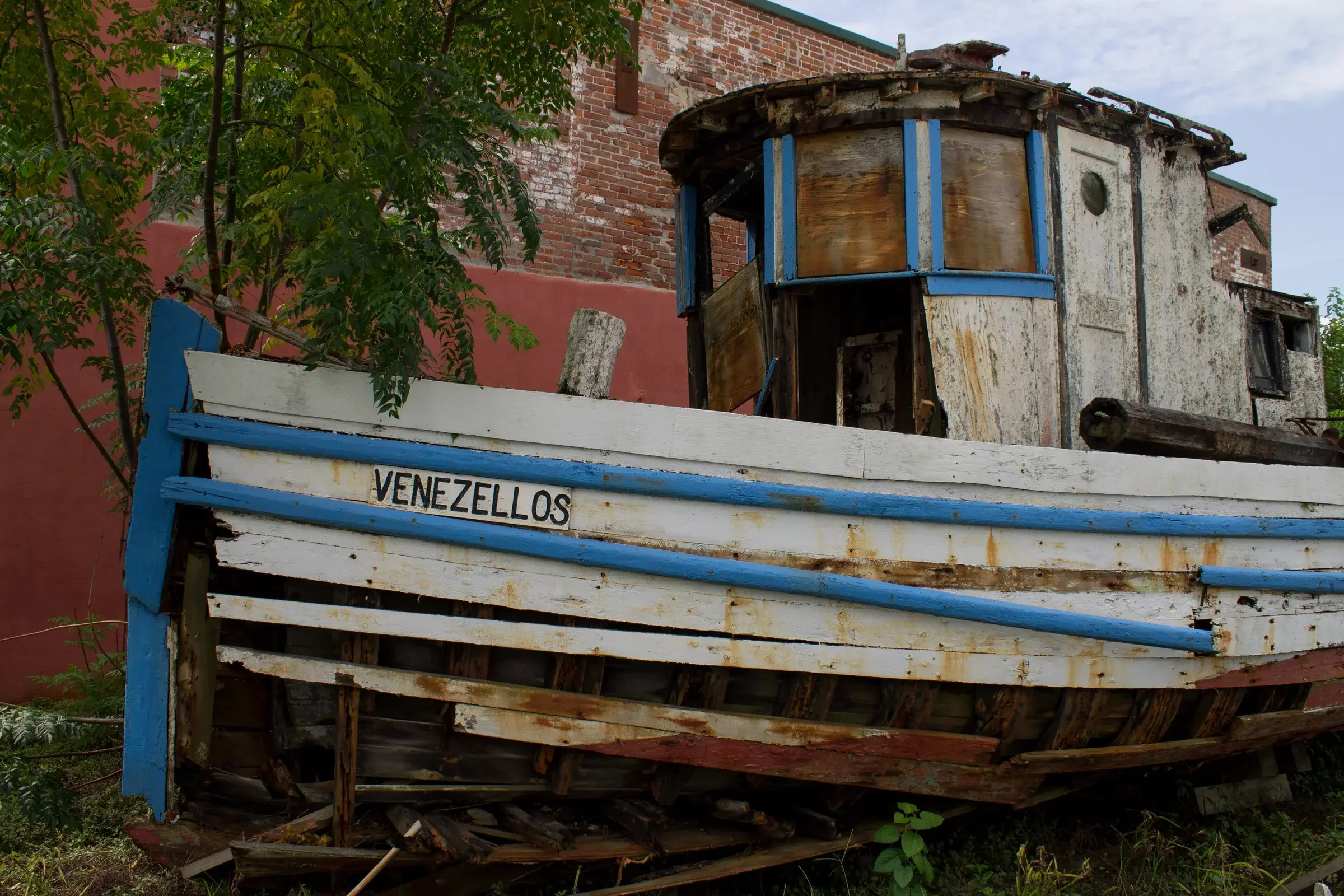 The wooden fishing boat Venezellos, laid up on blocks against a brick wall on Avenue E.