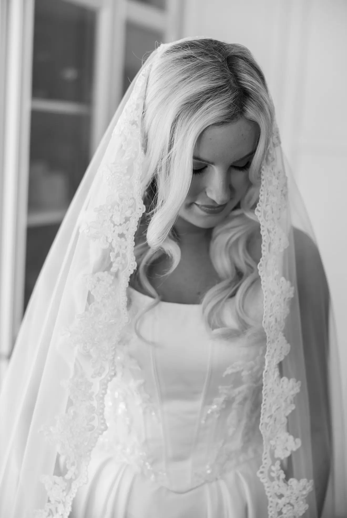 A bride in a lace-edged veil, photographed in black and white.