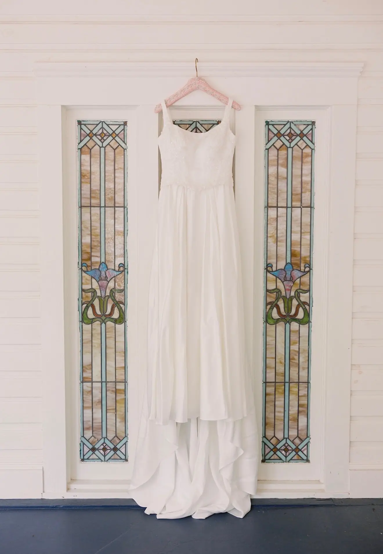 A wedding dress hanging against the original stained glass at 11 Mile.