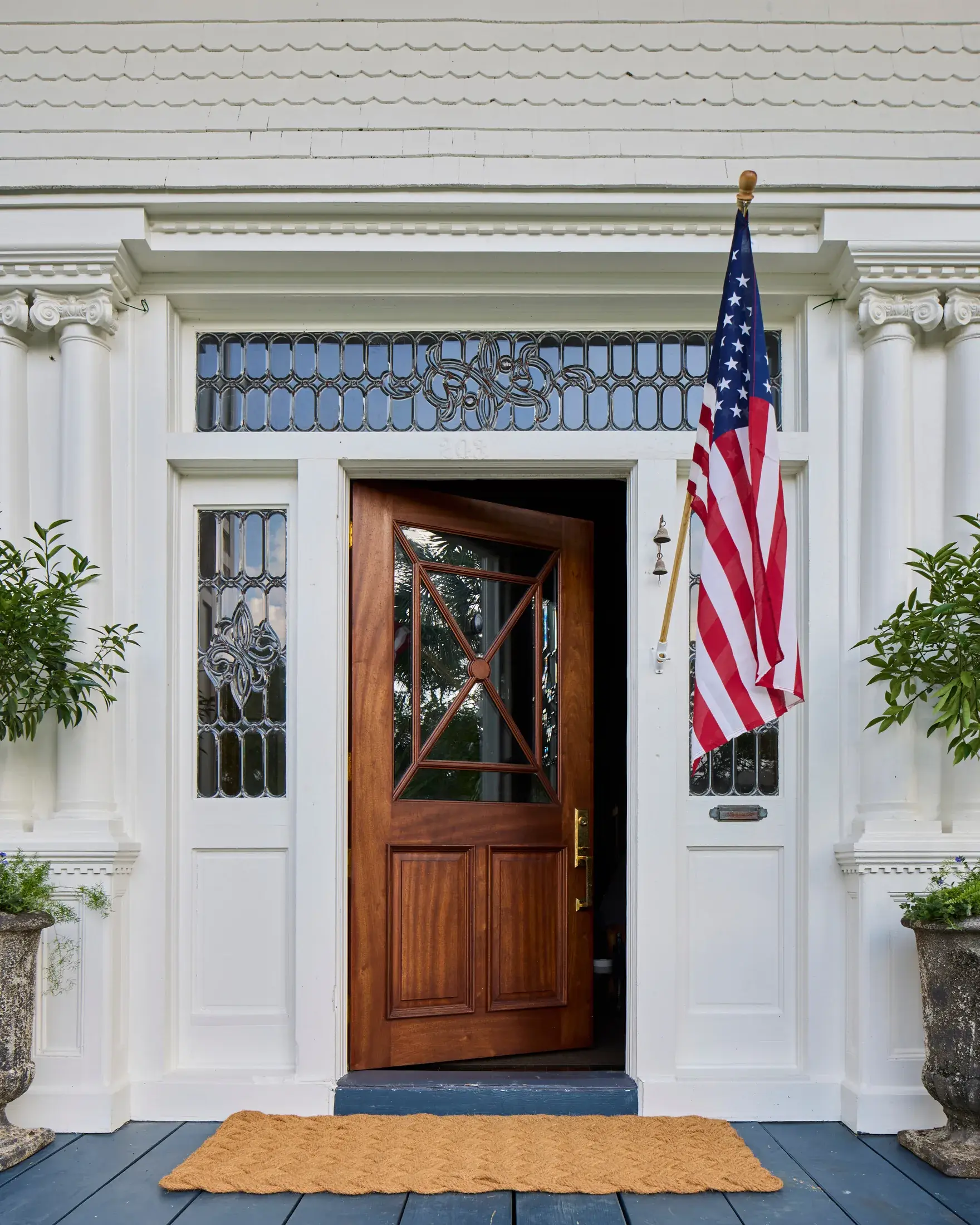 The front door in polished mahogany under a leaded glass transom, flanked by carved capitals and leaded sidelights.