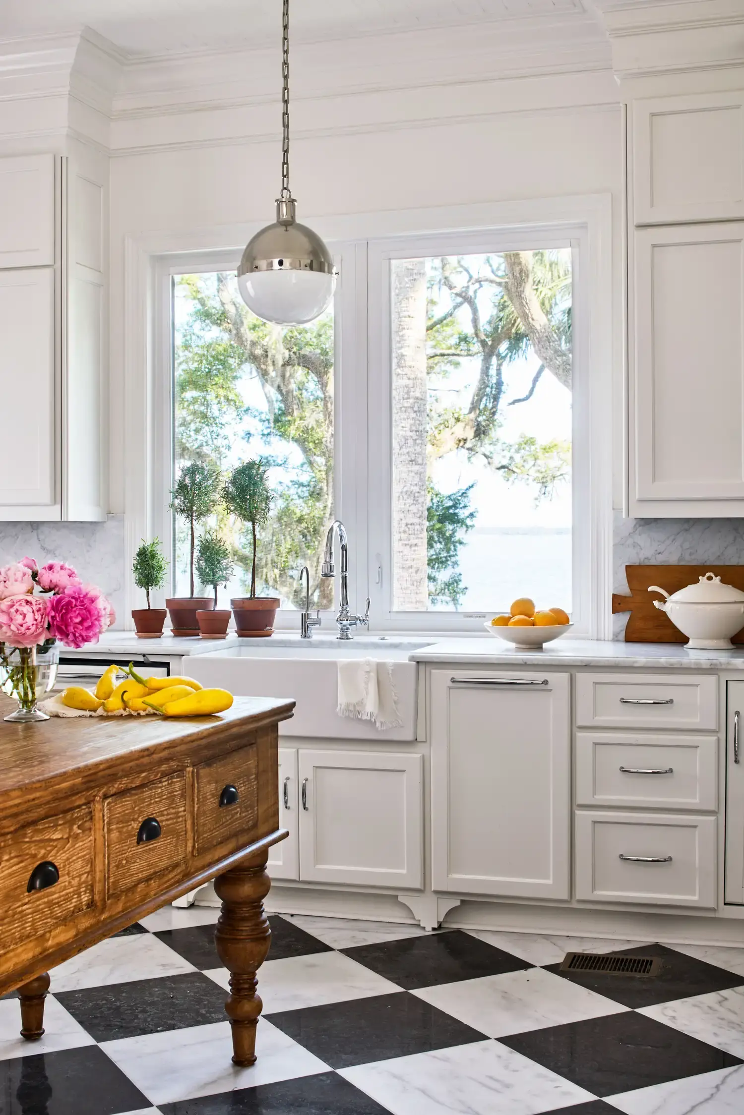 The kitchen: marble checkerboard floor, white cabinetry, an antique wooden island, and a window over the sink looking to the water.