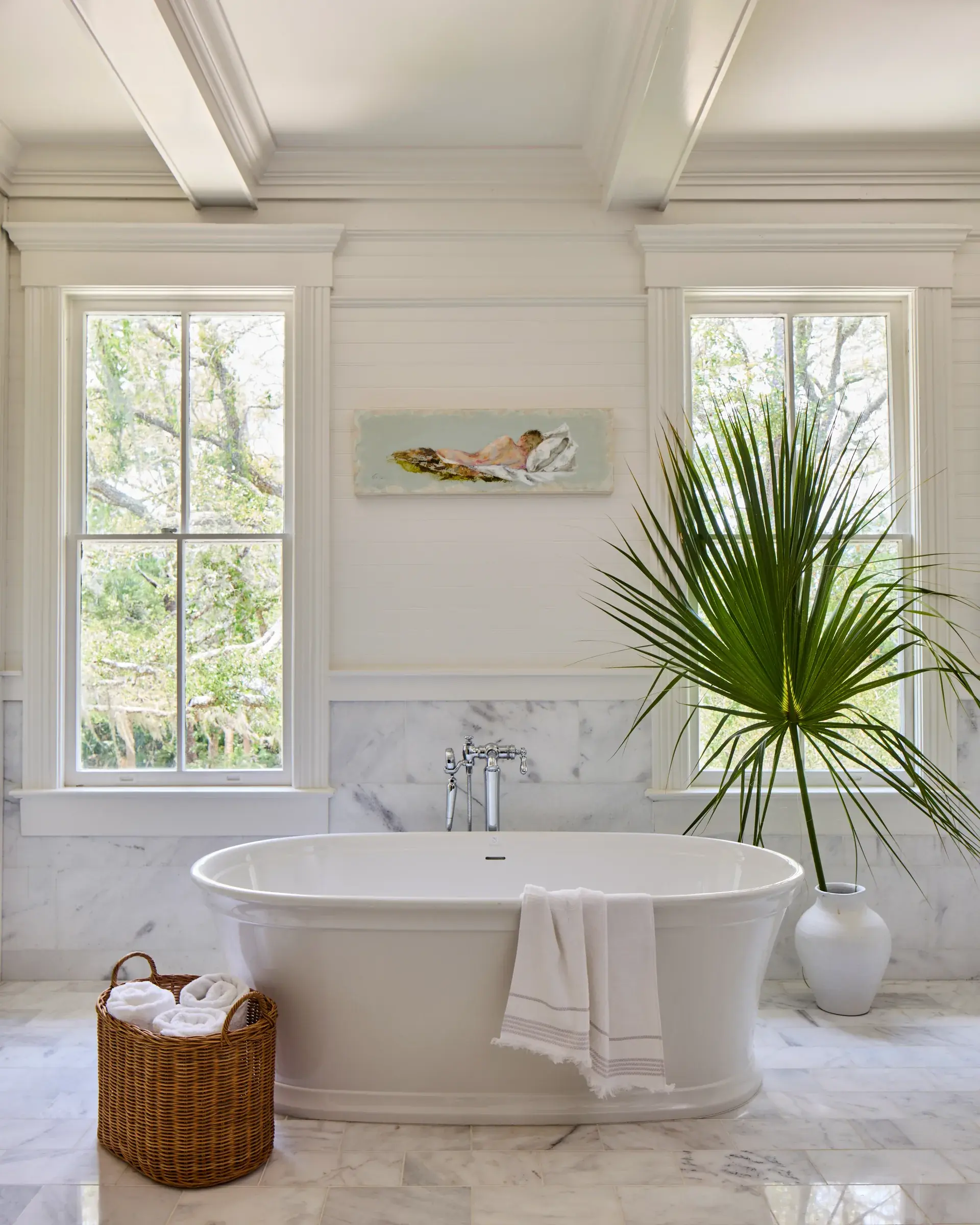 The principal bathroom: a freestanding tub against marble tile, two sash windows onto the oaks, and a coffered ceiling.
