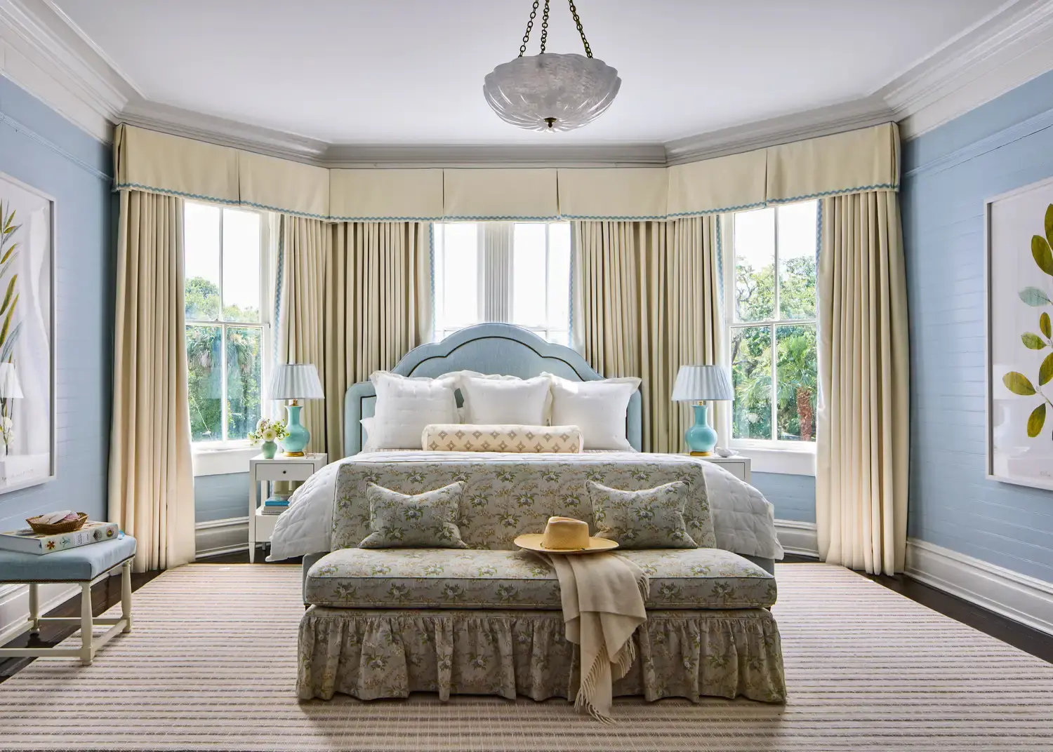The principal bedroom, pale blue walls, a bay window with full-length curtains, and an upholstered bed.